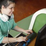 Asian young blind woman with headphone using computer with refreshable braille display or braille terminal a technology device for persons with visual disabilities.